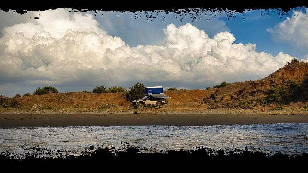 Un 4x4 acampando en la orilla del mar en una playa de Albania durante una ruta 4x4 por los Balcanes.