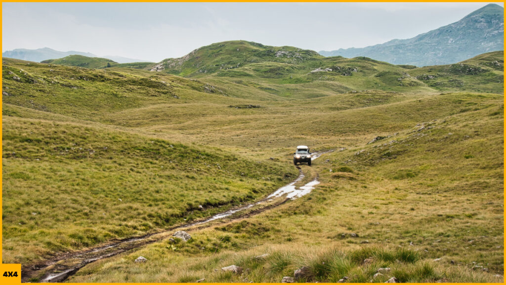 Un 4x4 conduciendo por una pista de barro entre prados verdes en Montenegro durante una ruta 4x4 por los Balcanes.