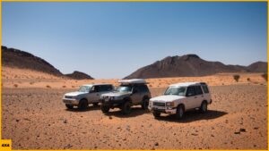 Tres 4x4 en un paisaje desértico de arena y montañas negras durante una ruta 4x4 por Marruecos.